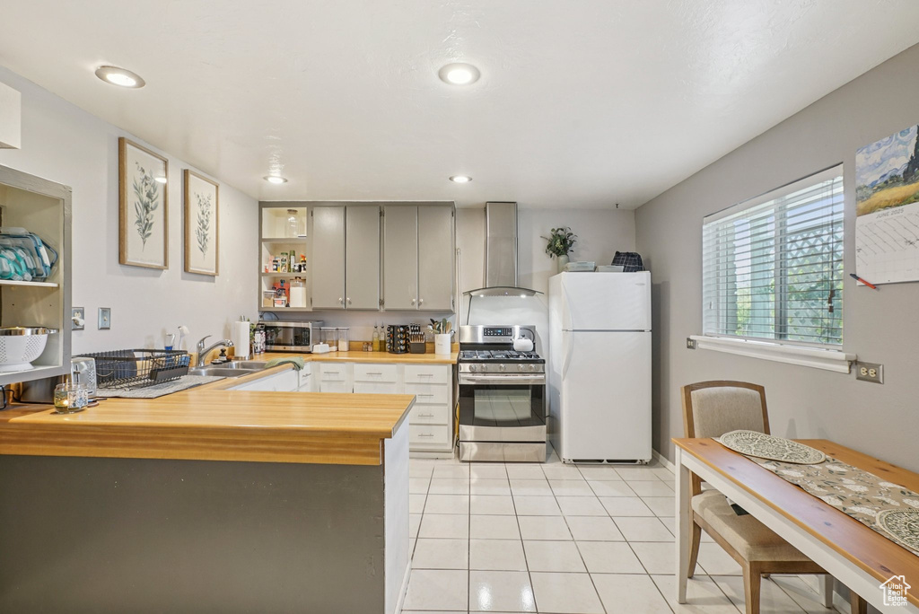Kitchen with appliances with stainless steel finishes, wall chimney exhaust hood, wood counters, light tile patterned floors, and a peninsula