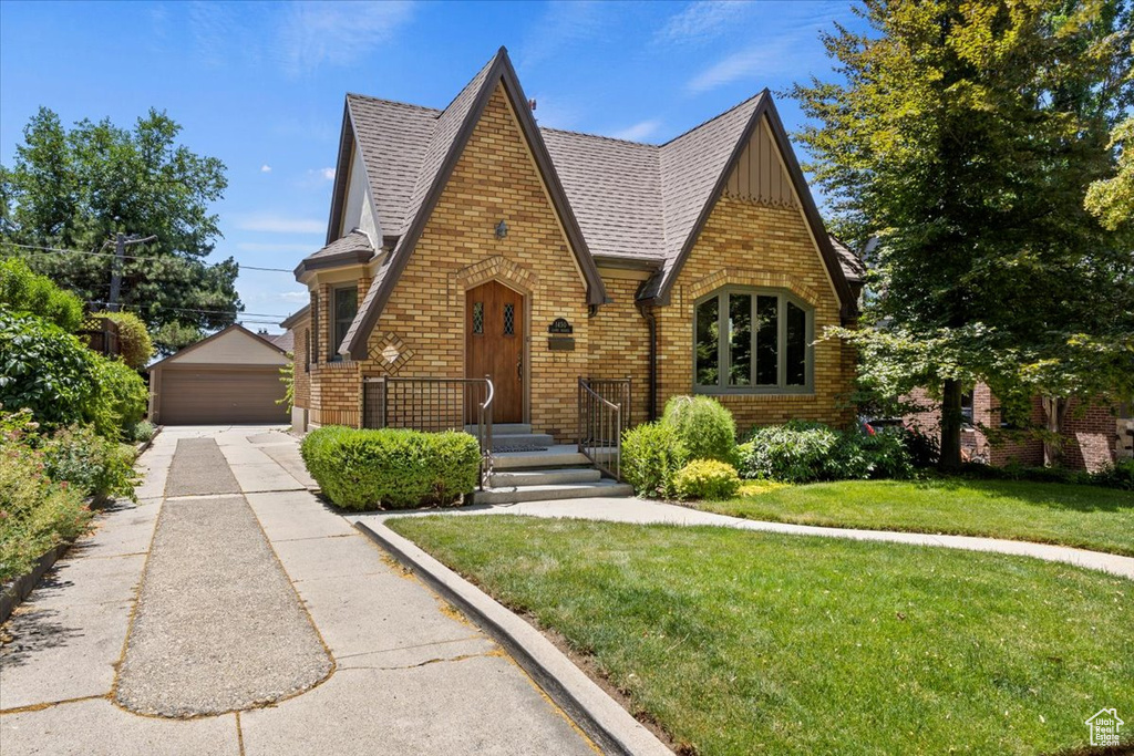 Tudor home with brick siding, a garage, a front yard, an outdoor structure, and board and batten siding