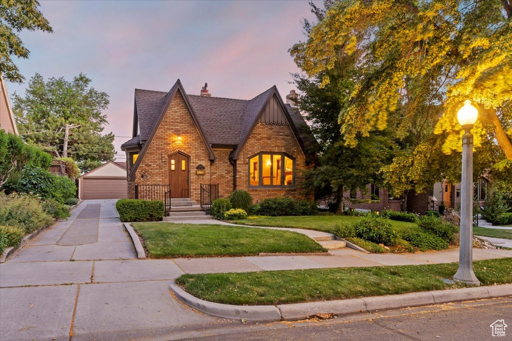 Tudor-style house with brick siding, an outdoor structure, a front yard, and a garage
