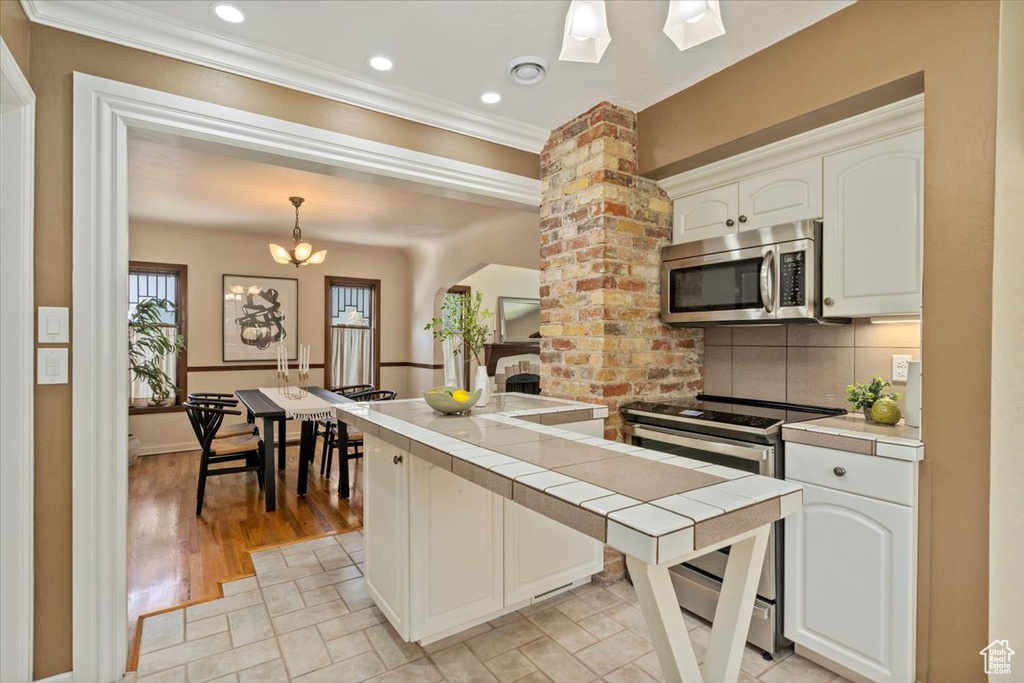 Kitchen with appliances with stainless steel finishes, tile countertops, backsplash, crown molding, and white cabinets