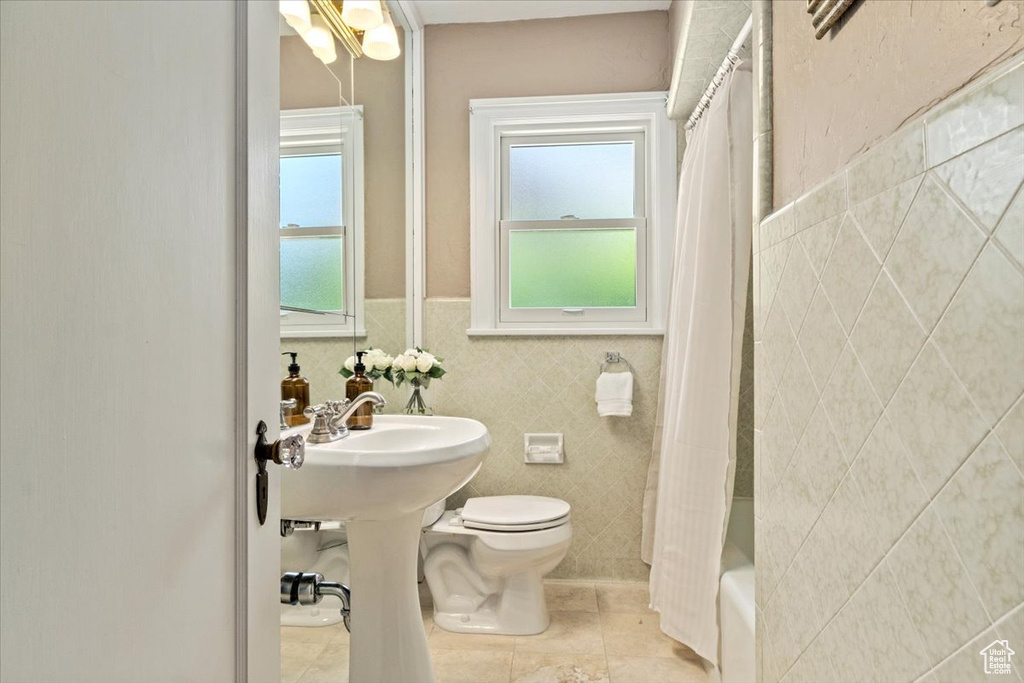 Full bath with tile walls, tile patterned flooring, shower / bathtub combination with curtain, and wainscoting