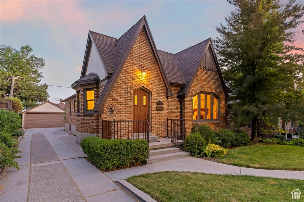Tudor house with a yard, a detached garage, a shingled roof, an outdoor structure, and brick siding