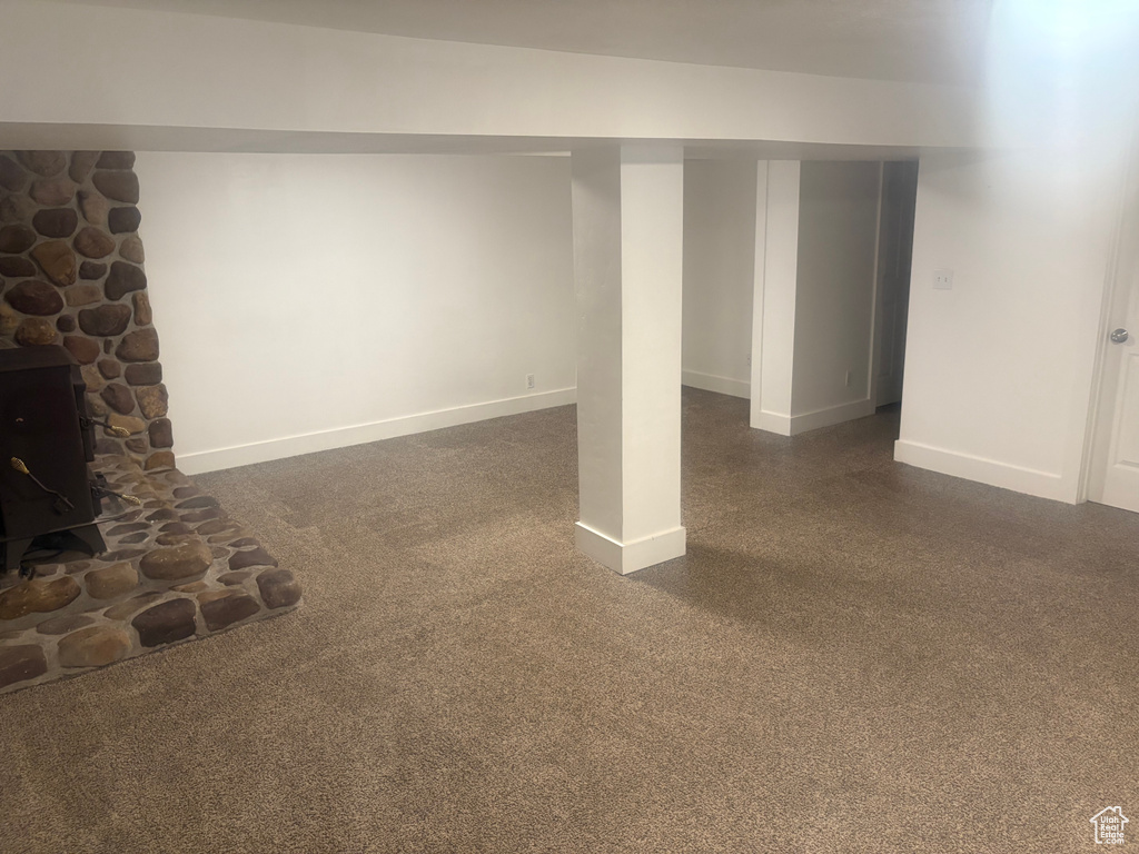 Finished basement featuring a wood stove and dark carpet