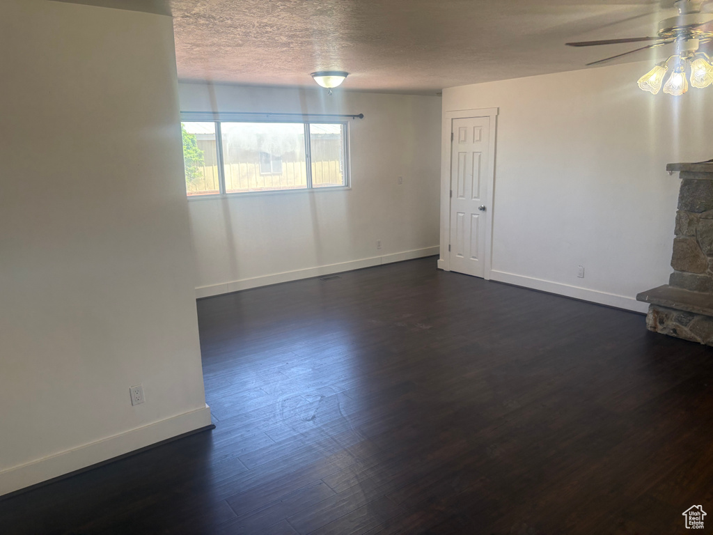 Unfurnished living room featuring ceiling fan, dark wood-type flooring, and a textured ceiling