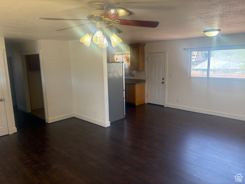 Unfurnished living room with a ceiling fan, a textured ceiling, and dark wood finished floors