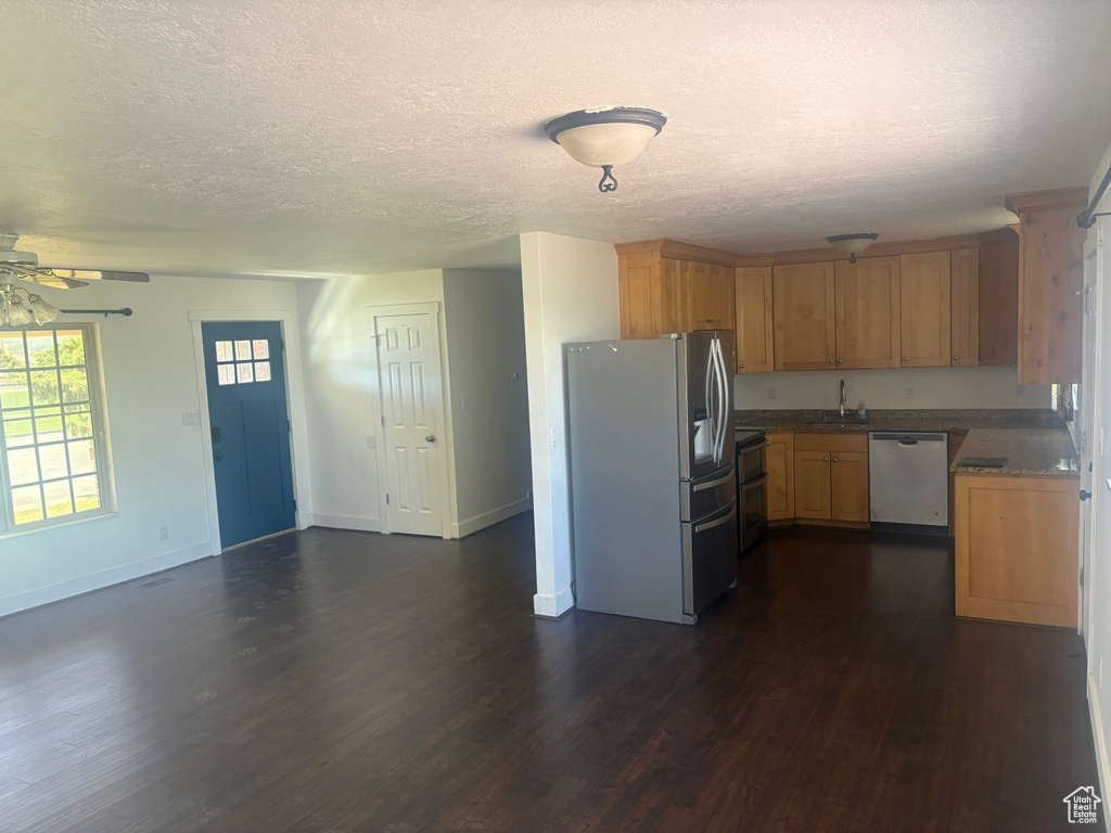 Kitchen with appliances with stainless steel finishes, dark wood-type flooring, a ceiling fan, and a textured ceiling