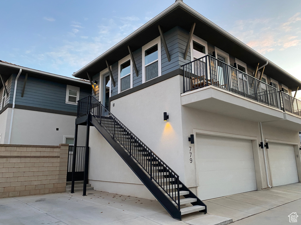 View of side of home with stucco siding, a garage, stairs, and a balcony
