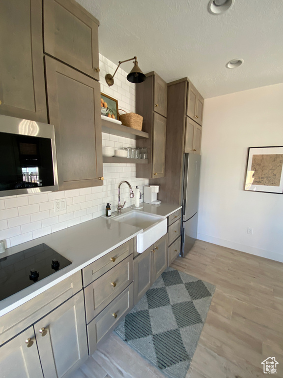 Kitchen featuring appliances with stainless steel finishes, open shelves, decorative backsplash, light countertops, and a textured ceiling