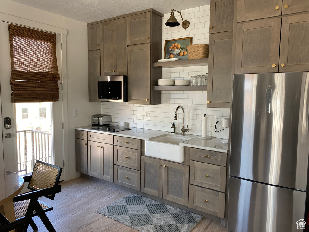 Kitchen with appliances with stainless steel finishes, tasteful backsplash, open shelves, light wood finished floors, and a textured ceiling