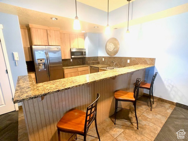 Kitchen featuring appliances with stainless steel finishes, light brown cabinets, a peninsula, decorative backsplash, and light stone counters
