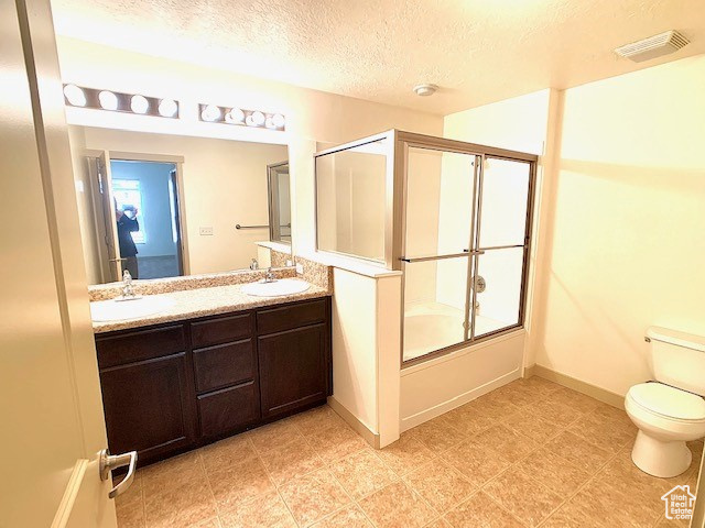 Bathroom featuring double vanity, a textured ceiling, and combined bath / shower with glass door