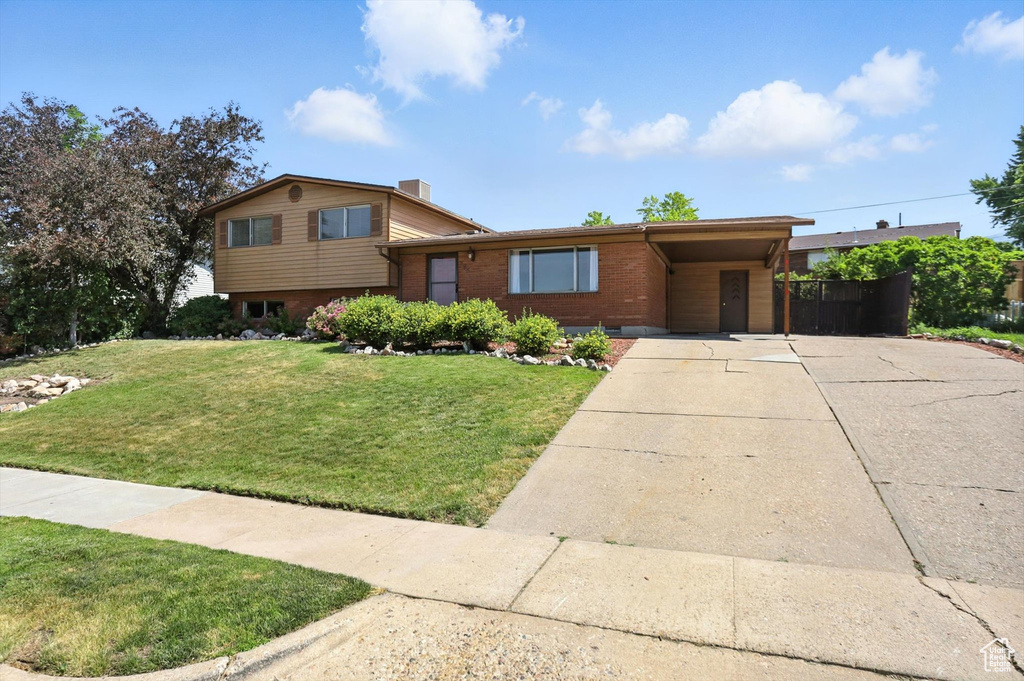 Split level home with brick siding, concrete driveway, a front lawn, and a carport