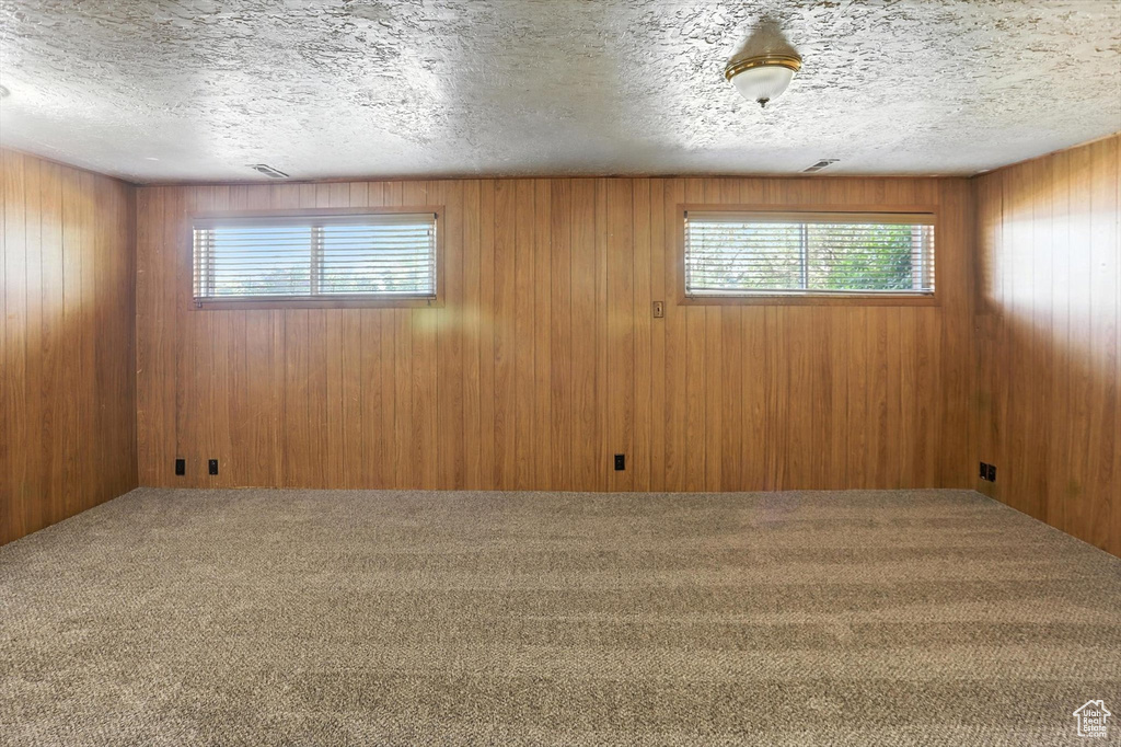 Spare room featuring carpet flooring, a textured ceiling, and wood walls