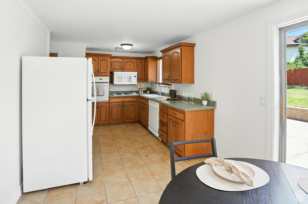 Kitchen with white appliances, brown cabinetry, plenty of natural light, and light tile patterned flooring