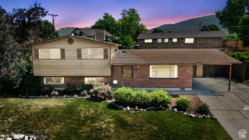 View of front facade featuring brick siding, an attached carport, concrete driveway, a front yard, and a mountain view