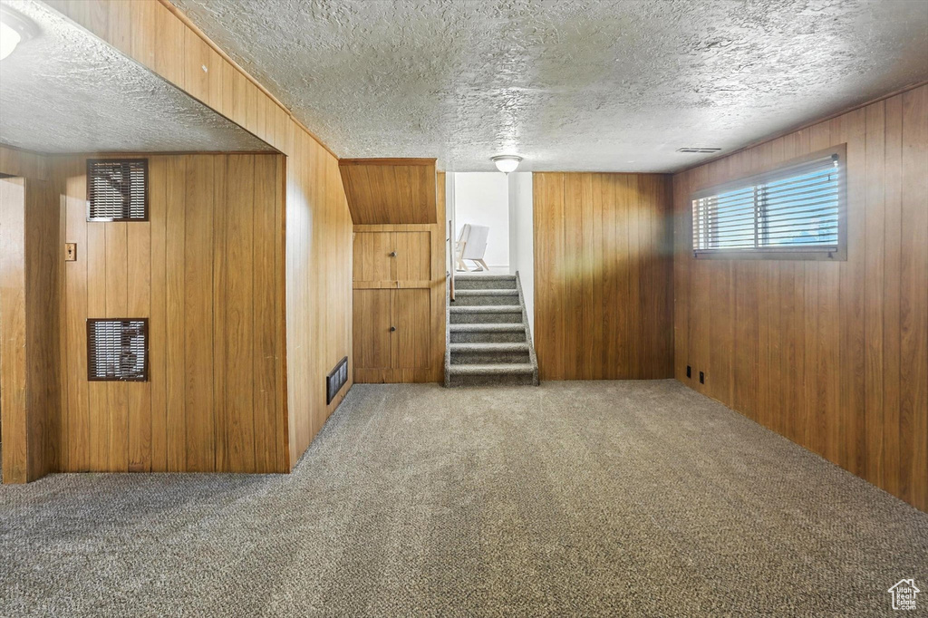 Below grade area featuring carpet floors, wood walls, stairway, and a textured ceiling