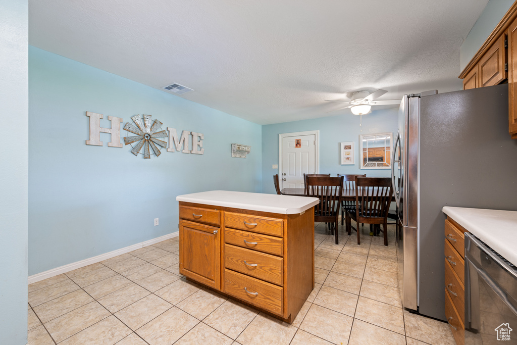 Kitchen with stainless steel appliances, brown cabinetry, light countertops, a ceiling fan, and light tile patterned floors