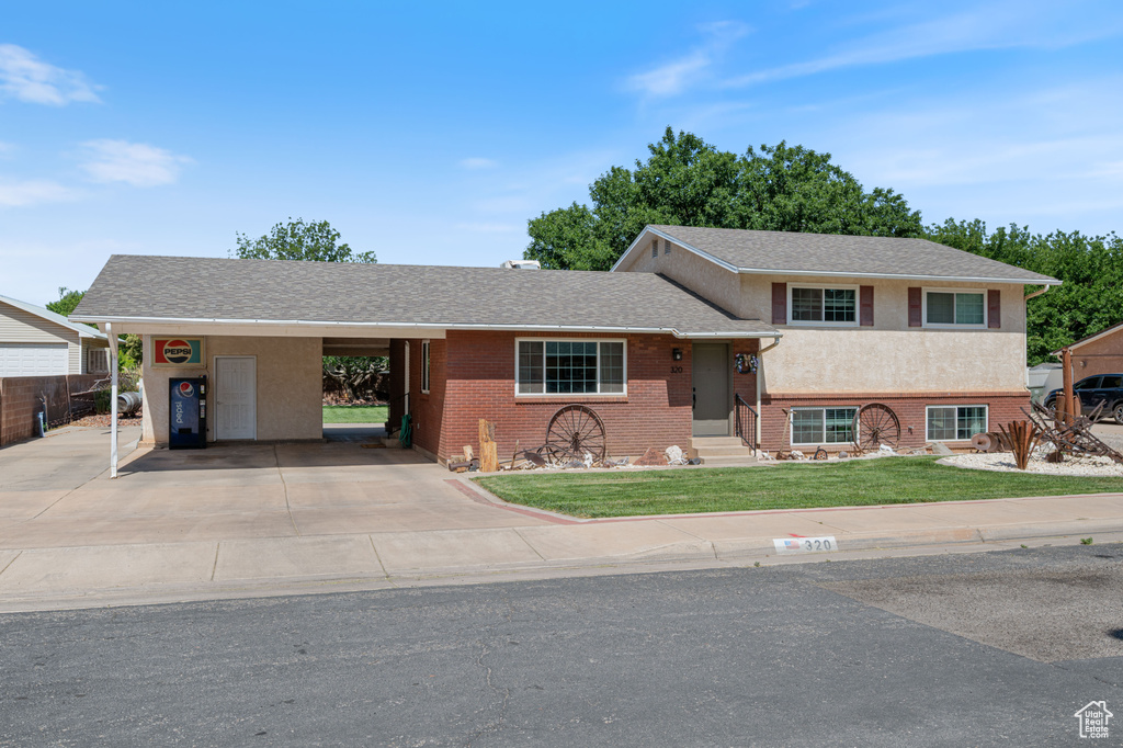 View of front of home with a front lawn, an attached carport, entry steps, driveway, and brick siding
