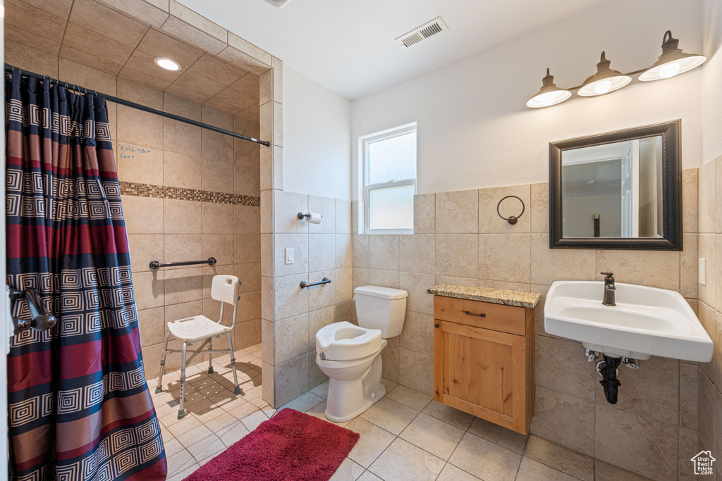 Full bath featuring tile walls, a tile shower, tile patterned floors, and a wainscoted wall