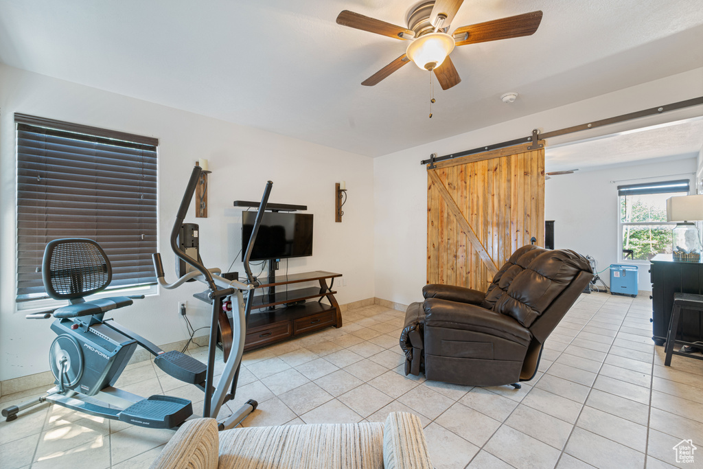 Workout area featuring a ceiling fan, light tile patterned floors, and a barn door
