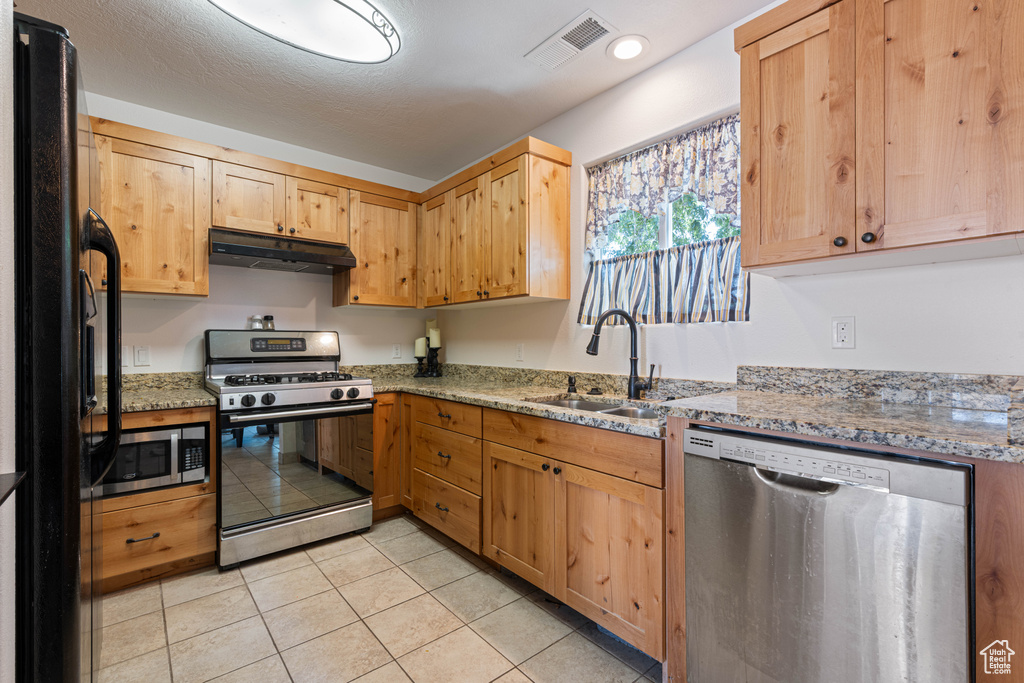 Kitchen featuring stainless steel appliances, under cabinet range hood, light tile patterned flooring, light stone counters, and light brown cabinetry