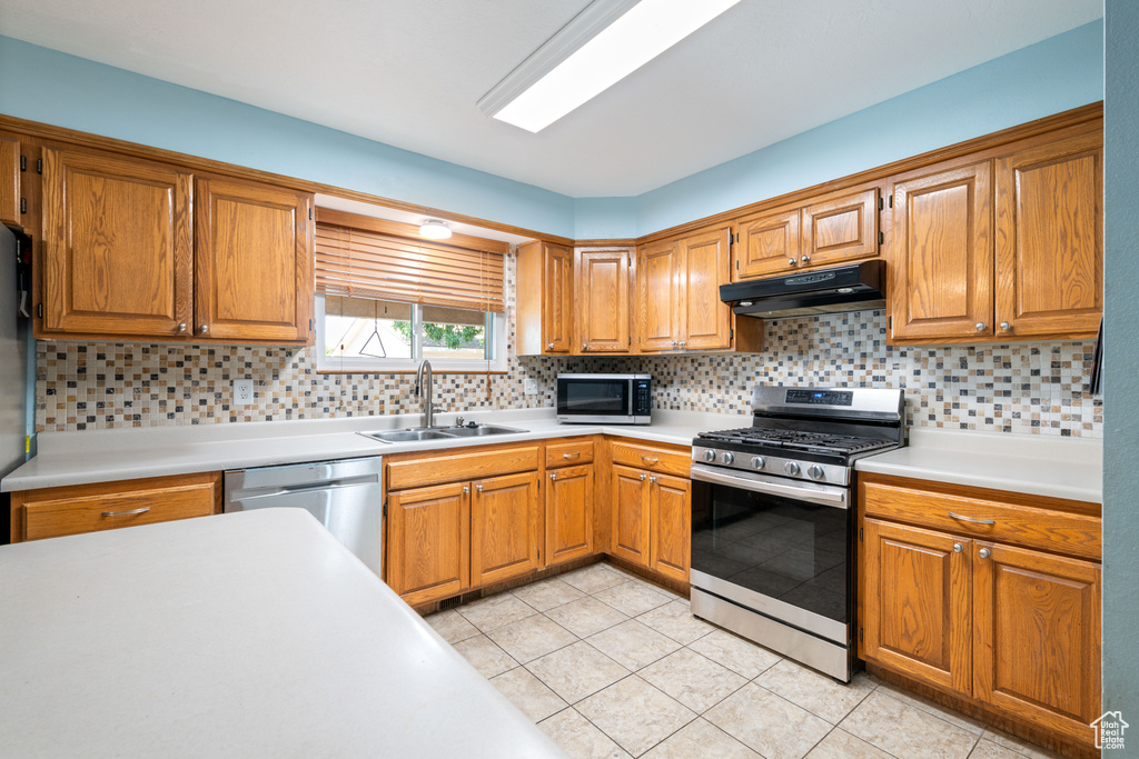 Kitchen with appliances with stainless steel finishes, under cabinet range hood, light countertops, and light tile patterned floors