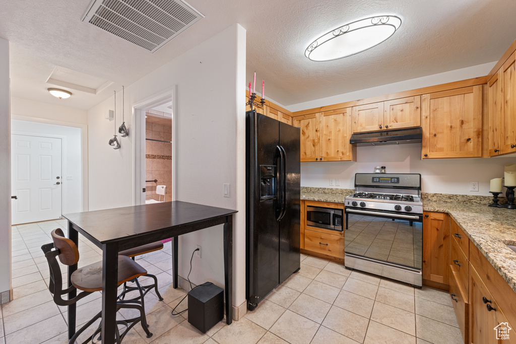 Kitchen featuring appliances with stainless steel finishes, under cabinet range hood, light tile patterned flooring, and light stone counters