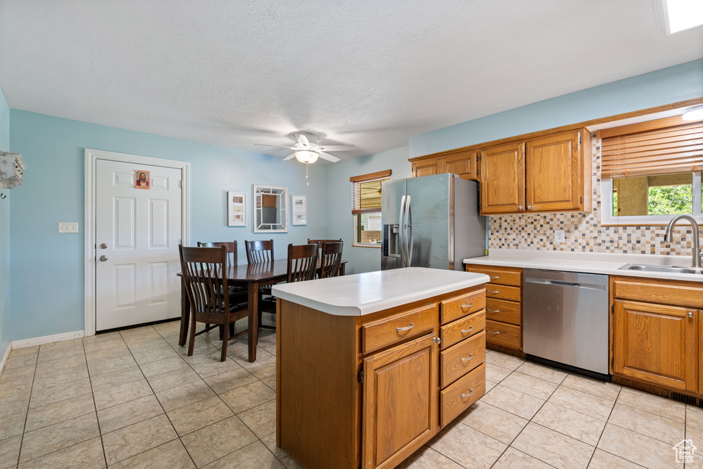 Kitchen featuring appliances with stainless steel finishes, a ceiling fan, backsplash, light countertops, and brown cabinets