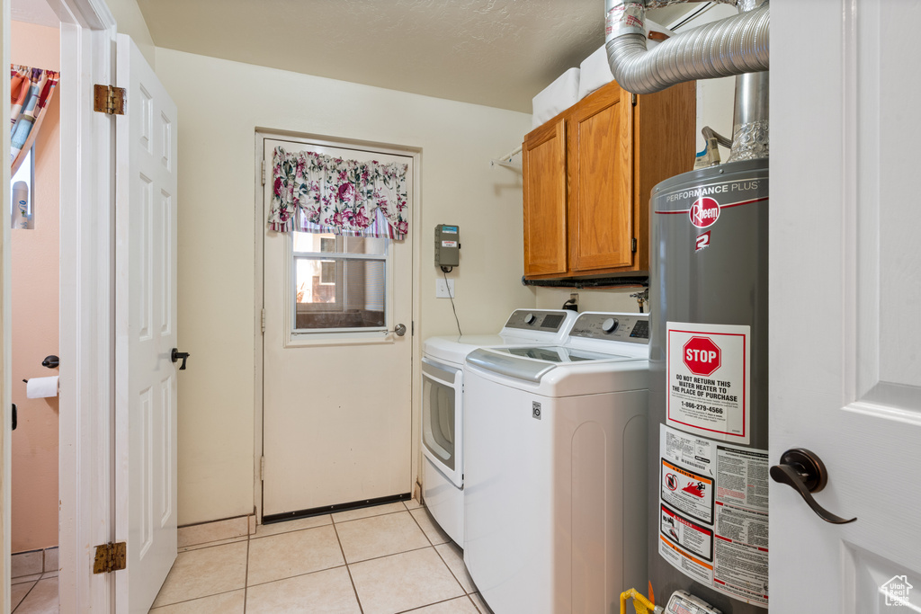 Washroom featuring cabinet space, gas water heater, washing machine and clothes dryer, and light tile patterned floors