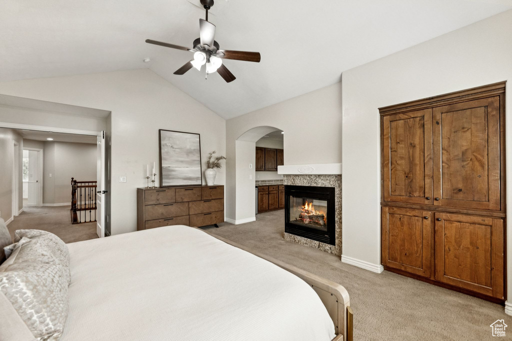 Bedroom with light colored carpet, lofted ceiling, arched walkways, a multi sided fireplace, and a ceiling fan