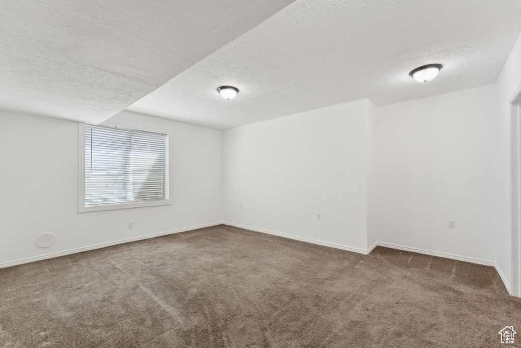 Carpeted empty room featuring a textured ceiling and baseboards