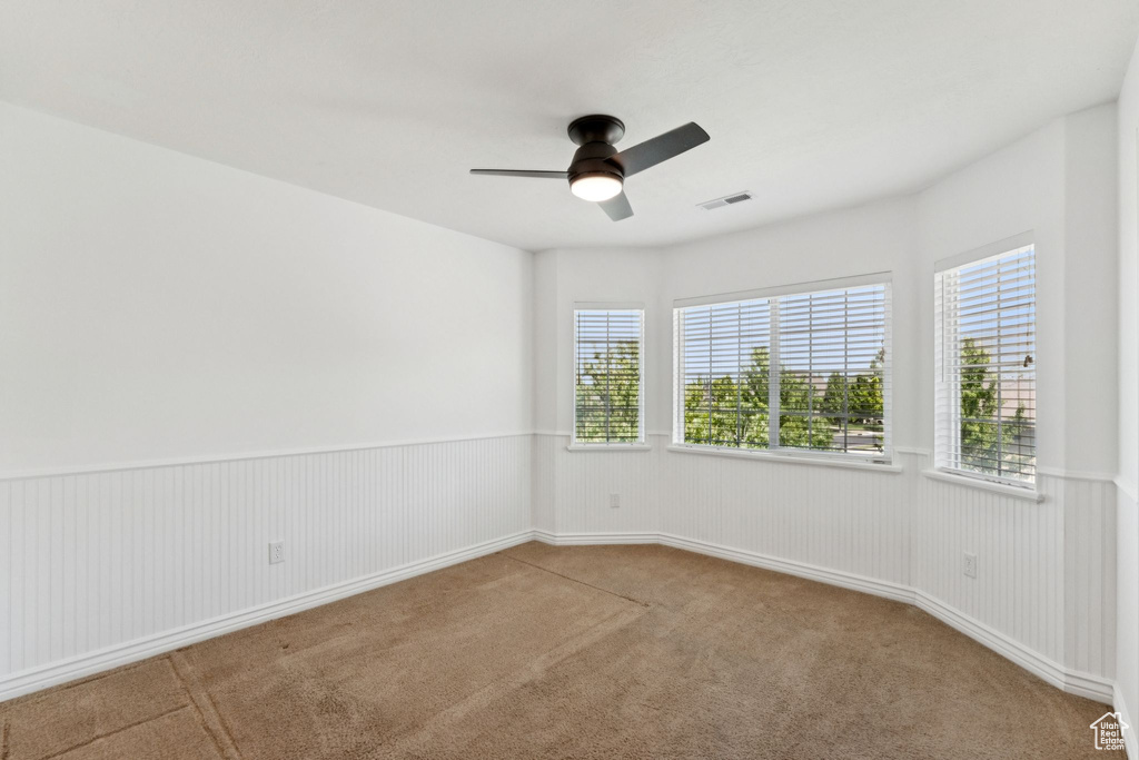 Unfurnished room featuring ceiling fan, carpet flooring, and wainscoting