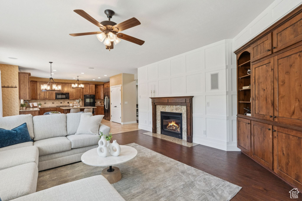 Living room with dark wood-type flooring, ceiling fan, a fireplace, a chandelier, and recessed lighting