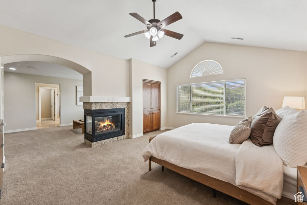 Carpeted bedroom with arched walkways, vaulted ceiling, a multi sided fireplace, and ceiling fan