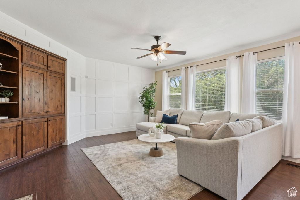 Living room featuring a decorative wall, plenty of natural light, ceiling fan, and dark wood-type flooring
