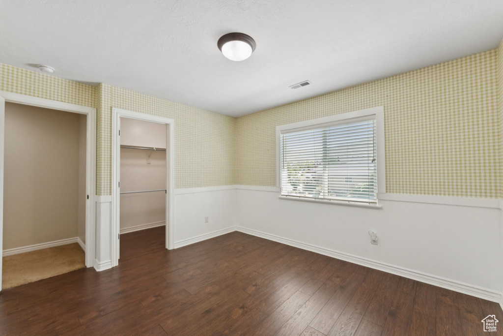 Unfurnished bedroom featuring wallpapered walls, a wainscoted wall, dark wood-style floors, a spacious closet, and a closet