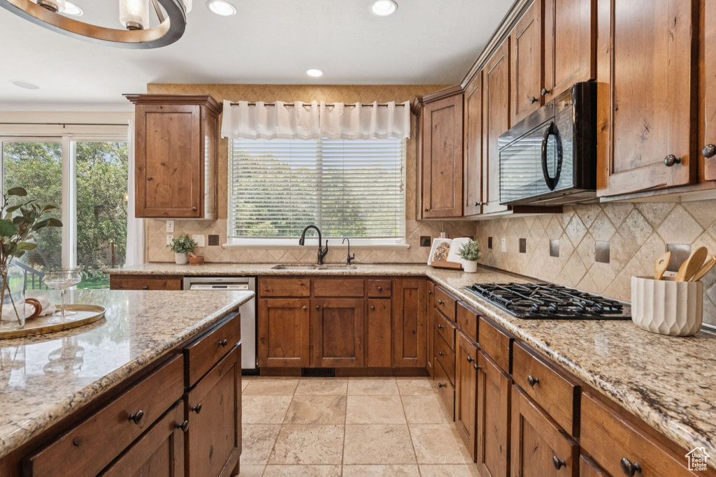 Kitchen featuring gas stovetop, stainless steel dishwasher, plenty of natural light, brown cabinetry, and recessed lighting
