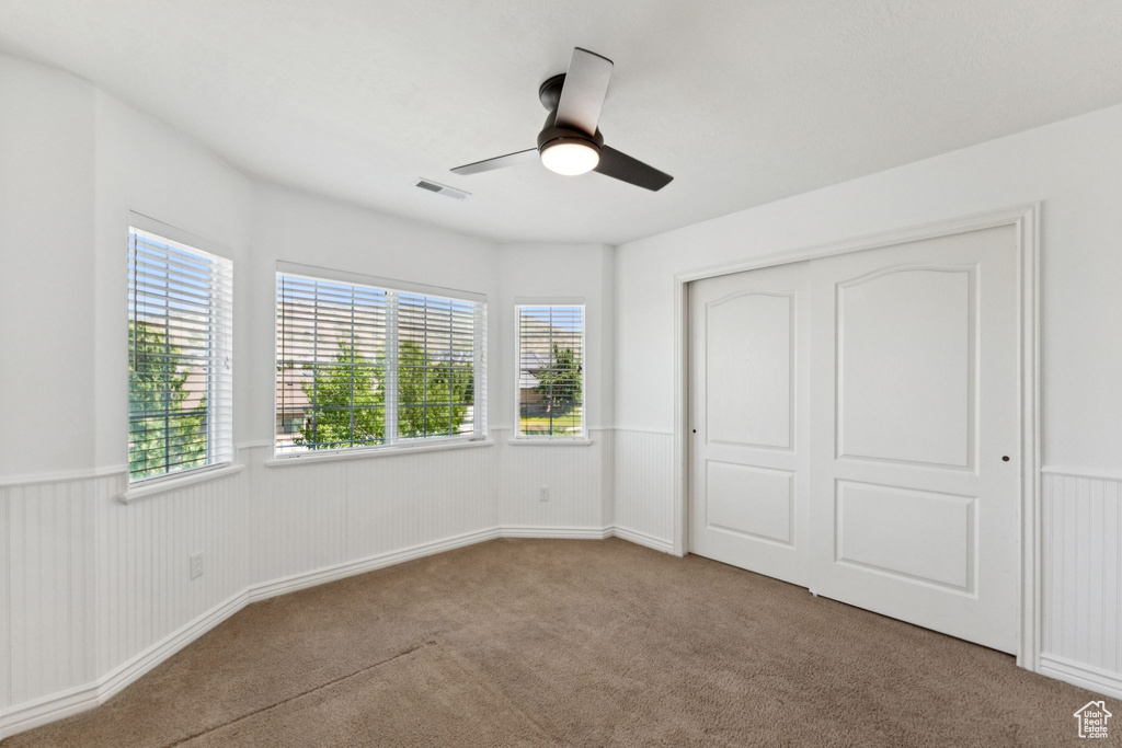 Unfurnished bedroom with carpet flooring, a closet, a ceiling fan, and a wainscoted wall
