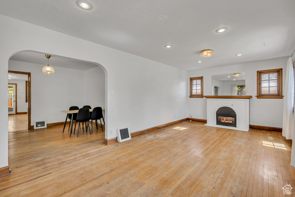 Unfurnished living room with arched walkways, light wood-style flooring, healthy amount of natural light, a glass covered fireplace, and recessed lighting