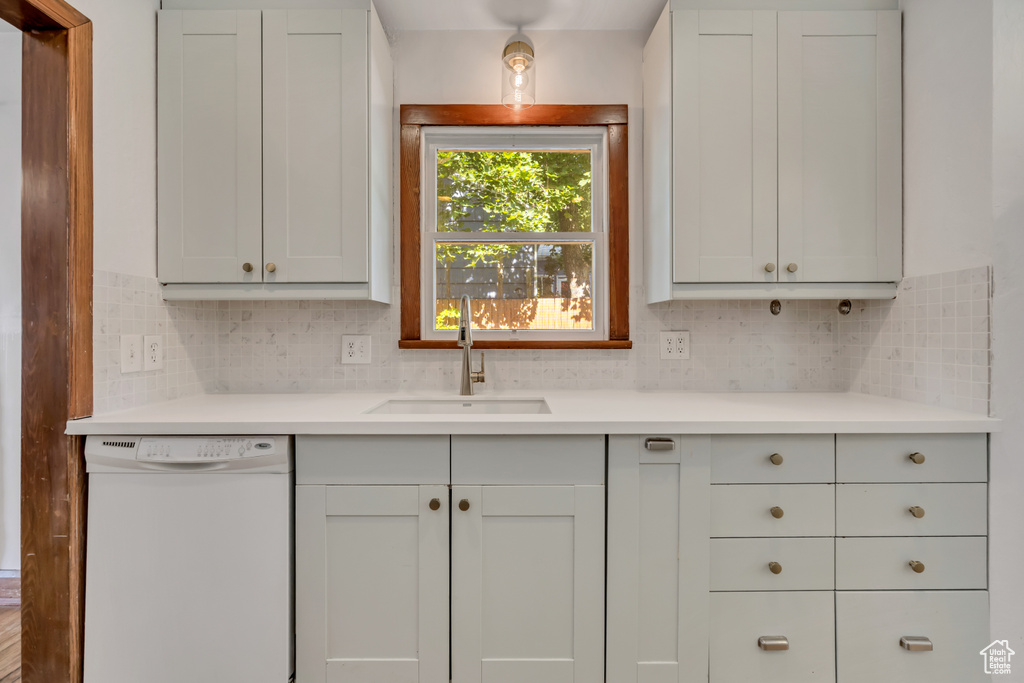 Kitchen with white dishwasher, tasteful backsplash, and light countertops