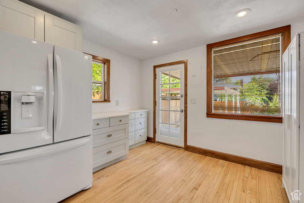 Kitchen featuring white refrigerator with ice dispenser, light wood-style floors, light countertops, recessed lighting, and white cabinets
