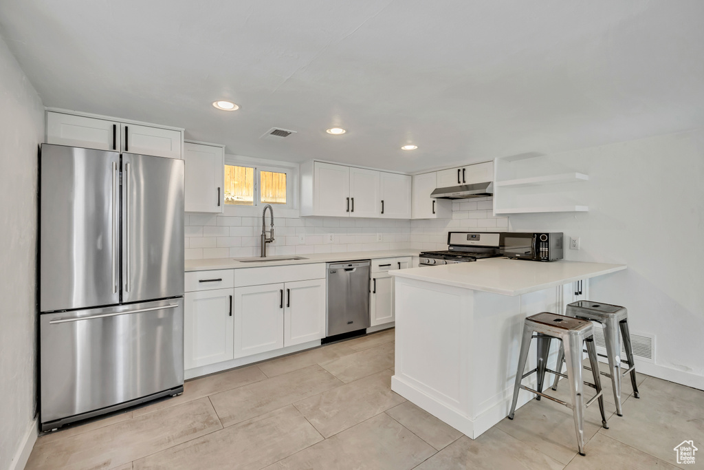 Kitchen with stainless steel appliances, under cabinet range hood, tasteful backsplash, white cabinets, and recessed lighting