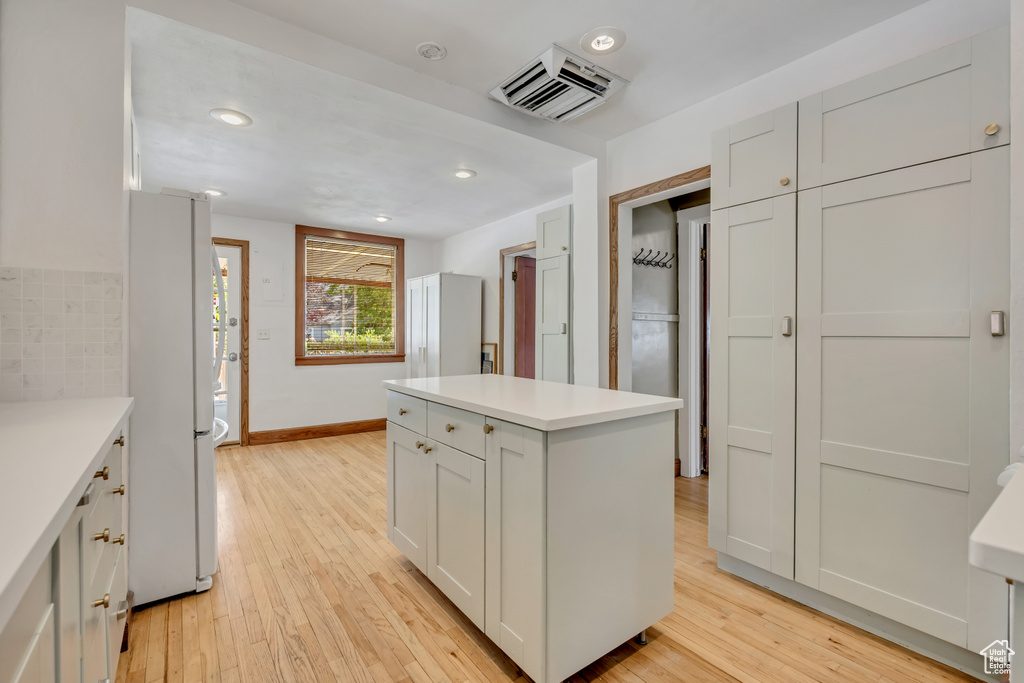 Kitchen with freestanding refrigerator, light wood-type flooring, light countertops, a center island, and recessed lighting
