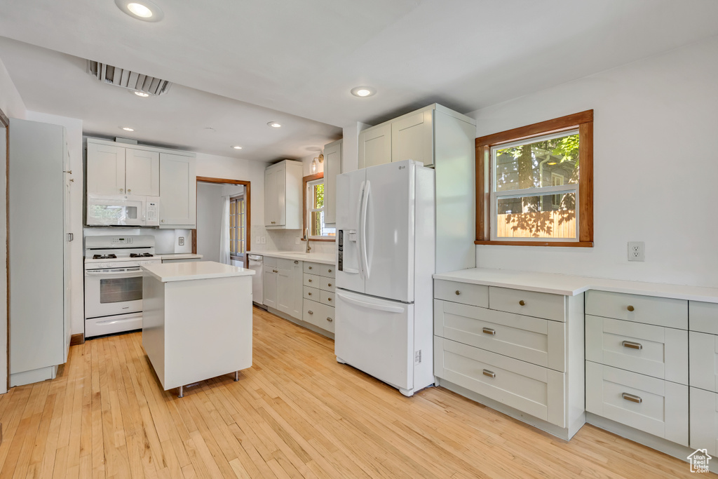 Kitchen with white appliances, light wood-style floors, light countertops, a center island, and recessed lighting