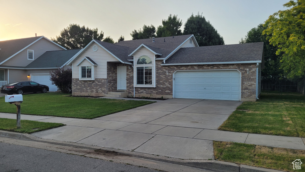 Ranch-style house featuring an attached garage, a yard, brick siding, and driveway