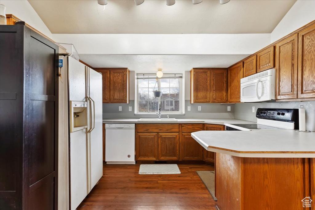 Kitchen featuring white appliances, brown cabinets, dark wood finished floors, and light countertops