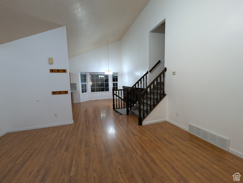 Interior space with a chandelier, wood finished floors, stairs, and high vaulted ceiling