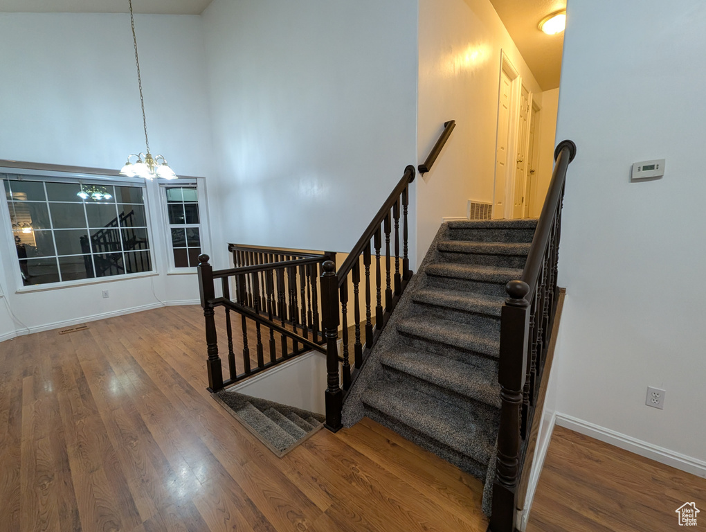 Staircase with a chandelier, wood finished floors, and a towering ceiling