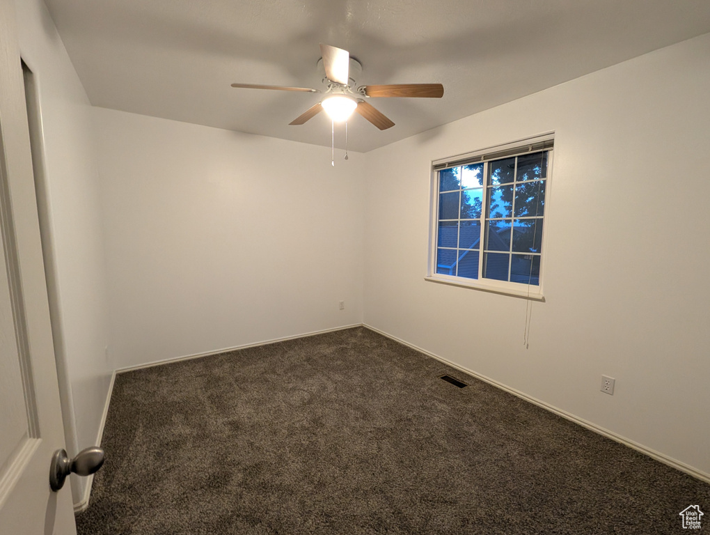 Empty room with dark carpet and a ceiling fan