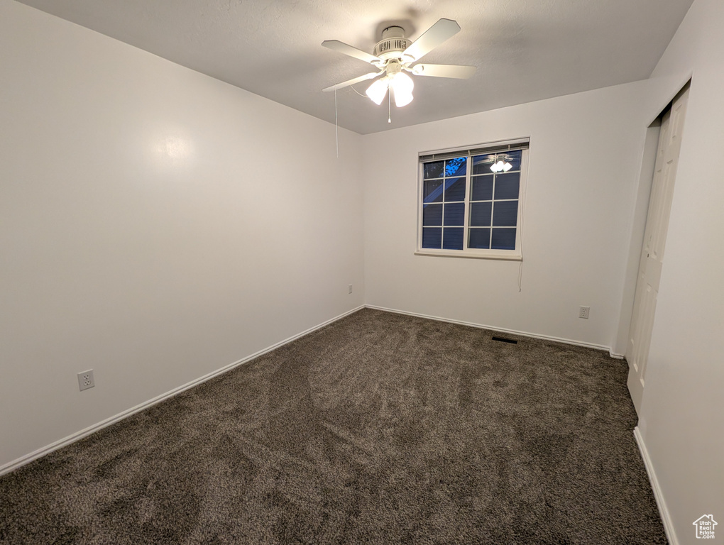 Spare room with dark carpet and a ceiling fan